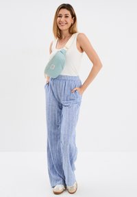Blauwe gestreepte wijde broek en een lichtblauwe schoudertas met rits. Het bovenstuk is een aansluitend wit tanktop. Sneakers zijn beige met witte accenten.