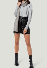 Haut à manches longues gris, shorts en simili cuir noir avec taille tie, et bottes noires montantes, associés à une écharpe légèrement grise en maille côtelée.