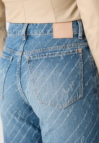 Vaqueros de denim de color azul claro con un diseño desvanecido y líneas diagonales. Incluye una etiqueta de cuero en la cintura y dos bolsillos traseros.
