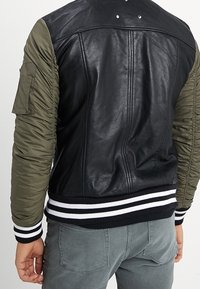 Veste bomber en cuir noir et nylon vert olive avec ourlet côtelé rayé, poche de style militaire et finition texturée.