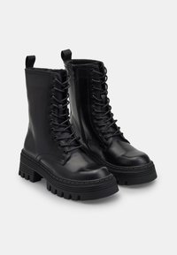 Botas de tobillo de cuero negro con suela de goma gruesa, diseño con cordones, cremallera lateral y tirador para facilitar su uso. Acabado texturizado.