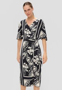 Robe portefeuille à motif de feuilles noir et blanc, manches courtes, décolleté en V et ceinture à la taille. Tissu lisse avec une coupe mi-longue.