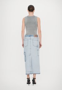 Siva rebrasta brezrokavna majica v kombinaciji s svetlo modrim jeans krilom, ki ima žepe s flapom, rob s frfotanjem in črne visoke petke.