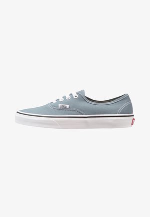 Zapatilla Vans baja azul con cordones blancos, suela de goma blanca y una franja negra sobre la suela, vista de lado.