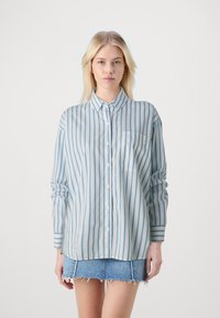 Light blue striped button-up shirt with long sleeves, featuring a chest pocket and a classic collar, paired with a denim mini skirt.