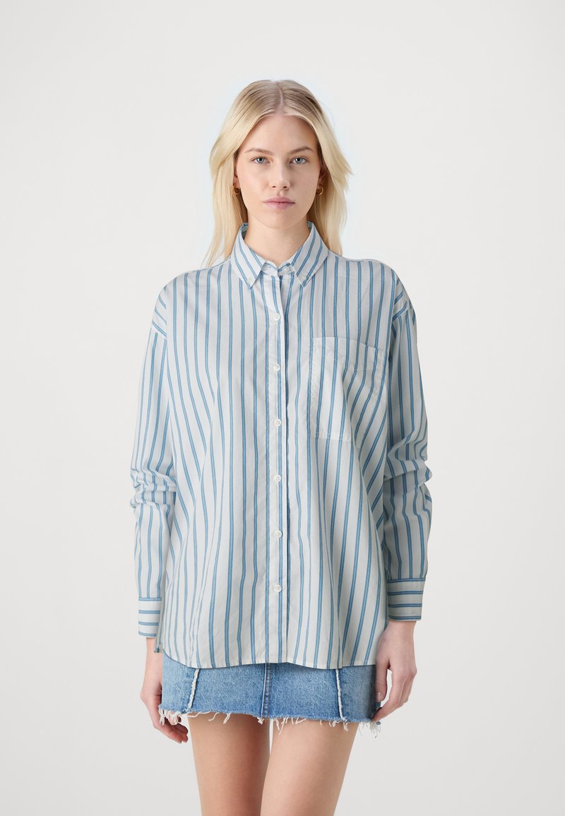 Light blue striped button-up shirt with long sleeves, featuring a chest pocket and a classic collar, paired with a denim mini skirt.