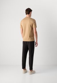 Lys beige kortermet t-skjorte i kombinasjon med svarte bukser og beige joggesko, med et enkelt design og myk tekstur.