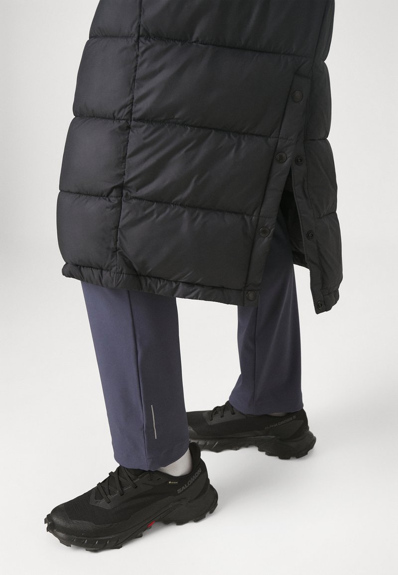 Abrigo de plumas negro con diseño acolchado y botones, combinado con pantalones azul marino con un acento plateado y zapatillas negras texturizadas.