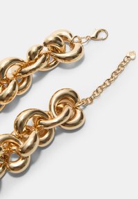 Armband aus goldfarbenen Kettengliedern mit glatten, abgerundeten Verbindungen. Der Verschluss ist ein Hummerverschluss mit einer Verlängerungskette. Polierte Oberfläche, ohne Muster.