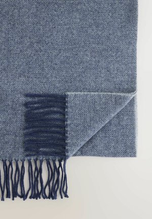 Blauwe deken met een visgraatpatroon en een gestructureerde afwerking; heeft een donkerblauwe franjerand langs één kant en een omgevouwen hoekdetail.