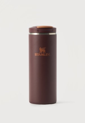 Un grand mug de voyage Stanley brun foncé, avec un couvercle assorti et un bouton supérieur couleur cuivre, sur un fond clair.