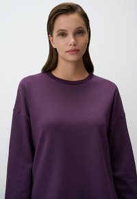 Felpa girocollo viola con vestibilità comoda, caratterizzata da maniche lunghe e un tessuto liscio e testurizzato, adatta per un abbigliamento casual.