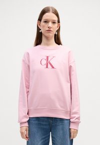 Sweatshirt in pile rosa con collo a giro e maniche lunghe, caratterizzato dal logo "Calvin Klein" in bianco e rosa scuro sulla parte anteriore.