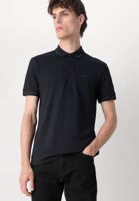 Μαύρο πόλο μπλουζάκι με κλασικό γιακά, κοντά μανίκια και διακριτικό λογότυπο "BOSS". Φτιαγμένο από λείο, ελαστικό ύφασμα με στενή εφαρμογή.