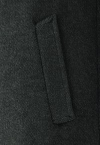 Dunkelgrüner Wollmantelstoff mit einer Nahaufnahme einer rechteckigen Tasche mit sauberer Naht. Die Textur ist leicht flauschig.