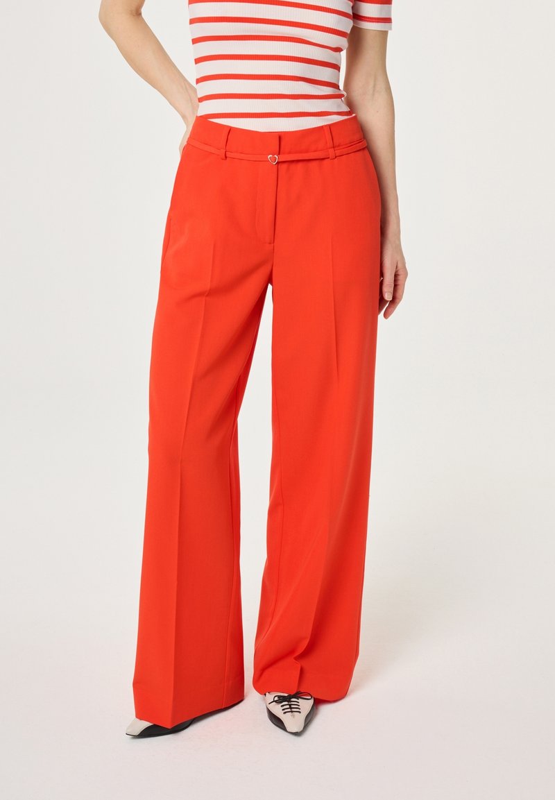 Woman wearing high-waist wide-leg red trousers with a slim matching belt and a white and red striped short-sleeve top.