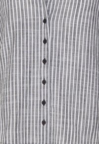 Button-up shirt in gestructureerde grijze stof met witte verticale strepen, voorzien van zwarte knopen en een V-hals ontwerp.