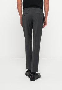 Gray dress pants with a straight leg design, back pockets with button closures, paired with black shoes and socks, viewed from the back.