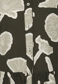 Abito in tessuto verde scuro con grandi motivi floreali bianchi, chiusura frontale a bottoni con bottoni di plastica azzurri e orlo arricciato.