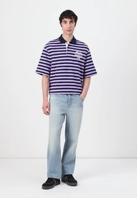 Lilla og svart stripete polo skjorte med krage, kombinert med lyseblå jeans og svarte joggesko. Skjorten har en logodetalj.