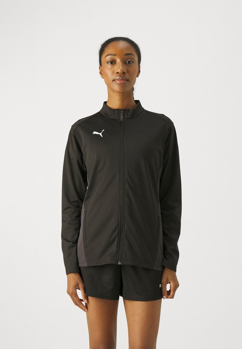 Svart zip-up jakke laget av lett stoff, med krage, sidelommer og en kontrasterende logo på brystet.