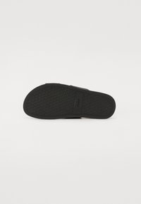 Chinelo noir avec une semelle en caoutchouc texturée, comportant une large bride et un logo près de la semelle intermédiaire. Fini lisse, design minimaliste.
