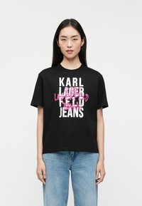 Camiseta de algodão preta com texto em branco em destaque e detalhes em rosa, combinada com jeans leves de corte largo em azul claro. Decote redondo simples e mangas curtas.