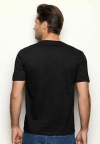 T-shirt in cotone nero con scollatura rotonda e maniche corte, vista da dietro. Il tessuto appare liscio con una vestibilità classica.