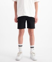 Zwarte shorts met een ritssluiting en zijvakjes, gedragen met witte sneakers en gestreepte crew-sokken, en een losse witte t-shirt.