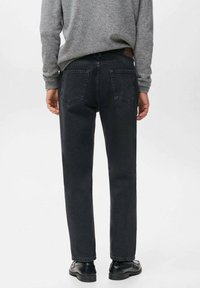 Jeans de mezclilla negra con un corte relajado, pierna recta y bolsillos traseros estructurados, combinados con un suéter gris y zapatos negros.