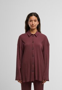 Burgunderfarget, ribbet skjorte med krage og lange ermer. Har en oversized passform og fem mørke knapper foran.