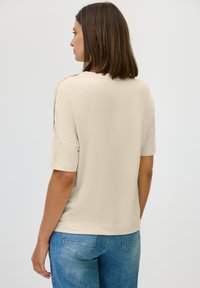 Beige T-shirt met korte mouwen van zachte stof, met een comfortabele pasvorm en een ronde halslijn, gecombineerd met blauwe spijkerbroek.