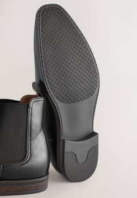 Zwarte leren enkellaarzen met elastische zijpanelen, een gestructureerde rubberen zool en een gladde afwerking. De hak heeft een subtiele accenten.