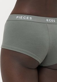 Sive pamučne hipster gaćice s bijelim "PIECES" logotipom na pojasu, s glatkom teksturom i prilagođenim dizajnom.