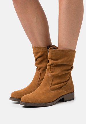 Brown suede ankle boots with a slouchy design, rounded toe, low wooden heel, and a side zipper, featuring stitching details.