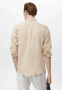 Beige long-sleeve shirt with a relaxed fit, button-down collar, and rolled sleeves, made of lightweight fabric, featuring a curved hemline.