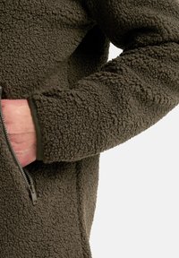 Braune Fleecejacke mit strukturiertem Außenmaterial, Reißverschluss-Tasche und eng anliegendem Bündchen. Weiches, warmes Material sorgt für Isolation und Komfort.