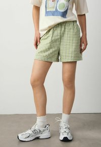Grønne og hvide gingham shorts med elastisk talje, parret med hvide sneakers og ribbede hvide sokker. Indstillingen er minimalistisch.
