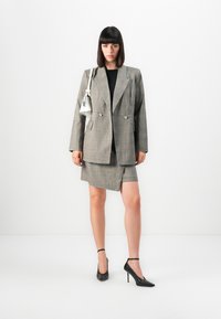 Grå rutete blazer med dobbelte knapper, kombinert med et matchende miniskjørt. Modellen har på seg en svart topp og sorte spisse hæler, og holder på en hvit håndveske.