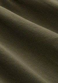 Olivgrüner Stoff mit einer glatten, leicht strukturierten Oberfläche, die feine Rippungen aufweist. Das Material zeigt weiche Falten und fällt natürlich.