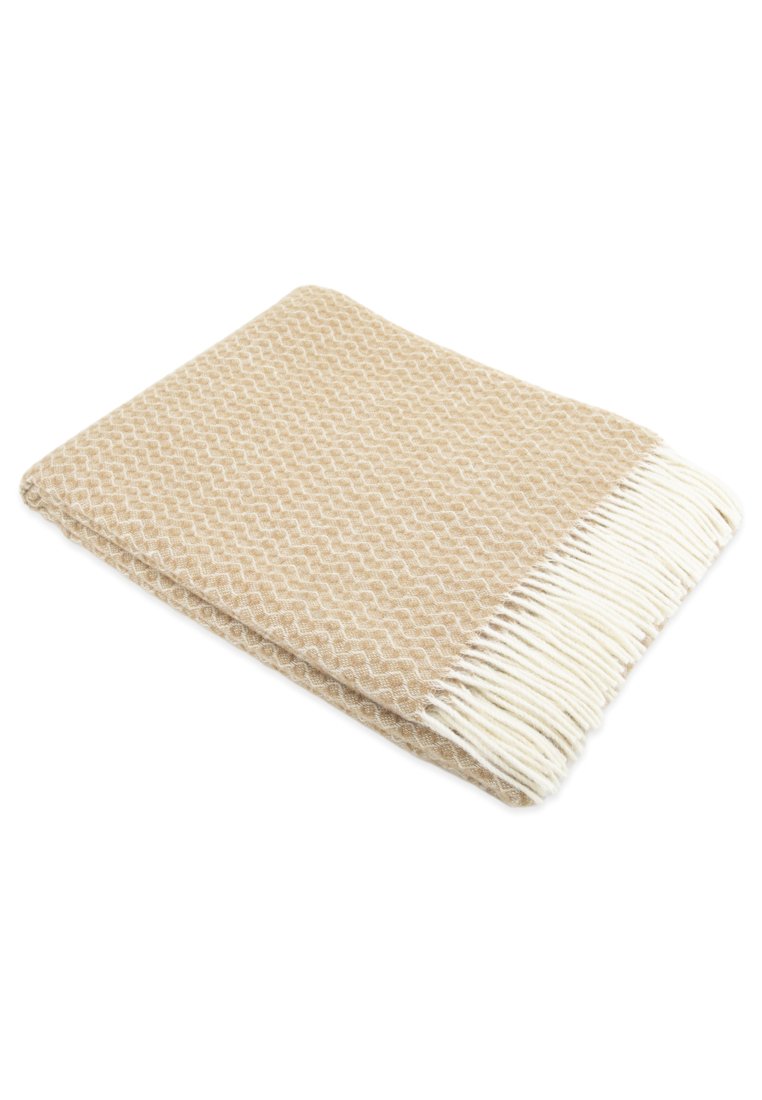 Manta de color beige tejida con un patrón de zigzag texturizado y bordes con flecos blancos, que muestra un acabado de tela suave.