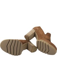 Hnědé nubukové kotníkové boty s robustním, texturovaným širokým podpatkem a gumovými podrážkami s vodorovnými drážkami pro lepší úchop.