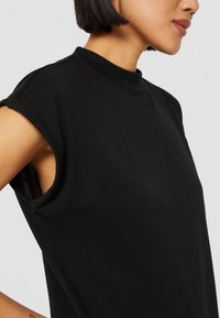 Svart höghalsskjorta med korta ärmar, tillverkad av mjukt tyg. Har en avslappnad passform och slät yta; minimalistisk design.