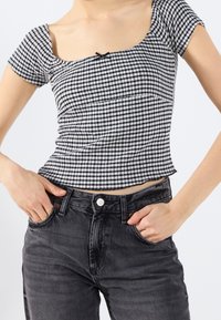 Black and white gingham print crop top with short sleeves and a square neckline, paired with high-waisted black denim jeans featuring a button closure.