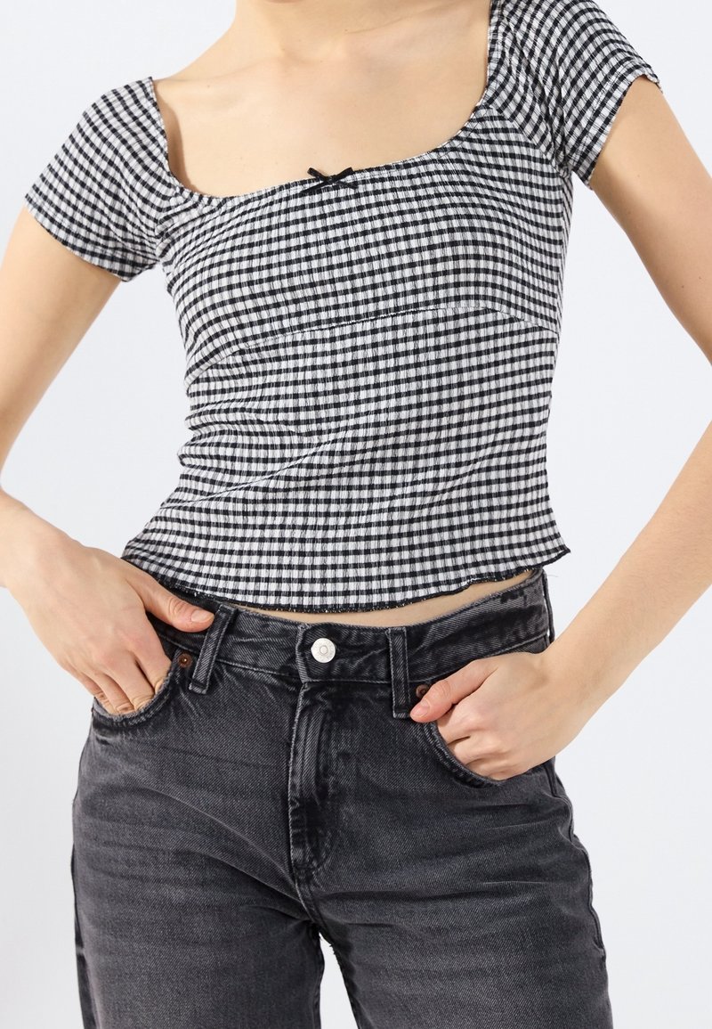 Black and white gingham print crop top with short sleeves and a square neckline, paired with high-waisted black denim jeans featuring a button closure.