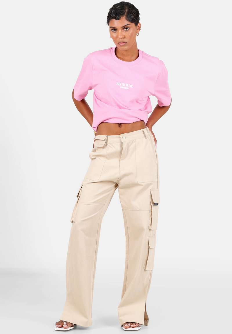 Roze cropped t-shirt met wit logo, gecombineerd met hoge beige cargobroek met meerdere zakken en een rechte pijp.