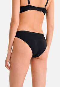 Bas de bikini noir en tissu lisse, avec une coupe taille mi-haute et une ceinture ornée du logo. Aucun motif ou texture supplémentaire visible.