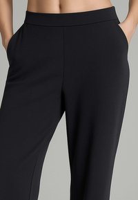 Pantaloni neri realizzati in tessuto morbido, con una cintura ampia e tasche laterali. Il design è rifinito con una gamba dritta.