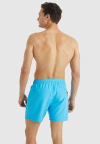 Jasně modré plavecké šortky vyrobené z lehkého materiálu, s elastickým pasem a boční kapsou. Hladká textura, délka nad kolena.
