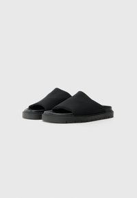 Sorte slip-on sko laget av stoff med en glatt tekstur, med åpen tå-design og en tykk gummisåle med et sporvet mønster.